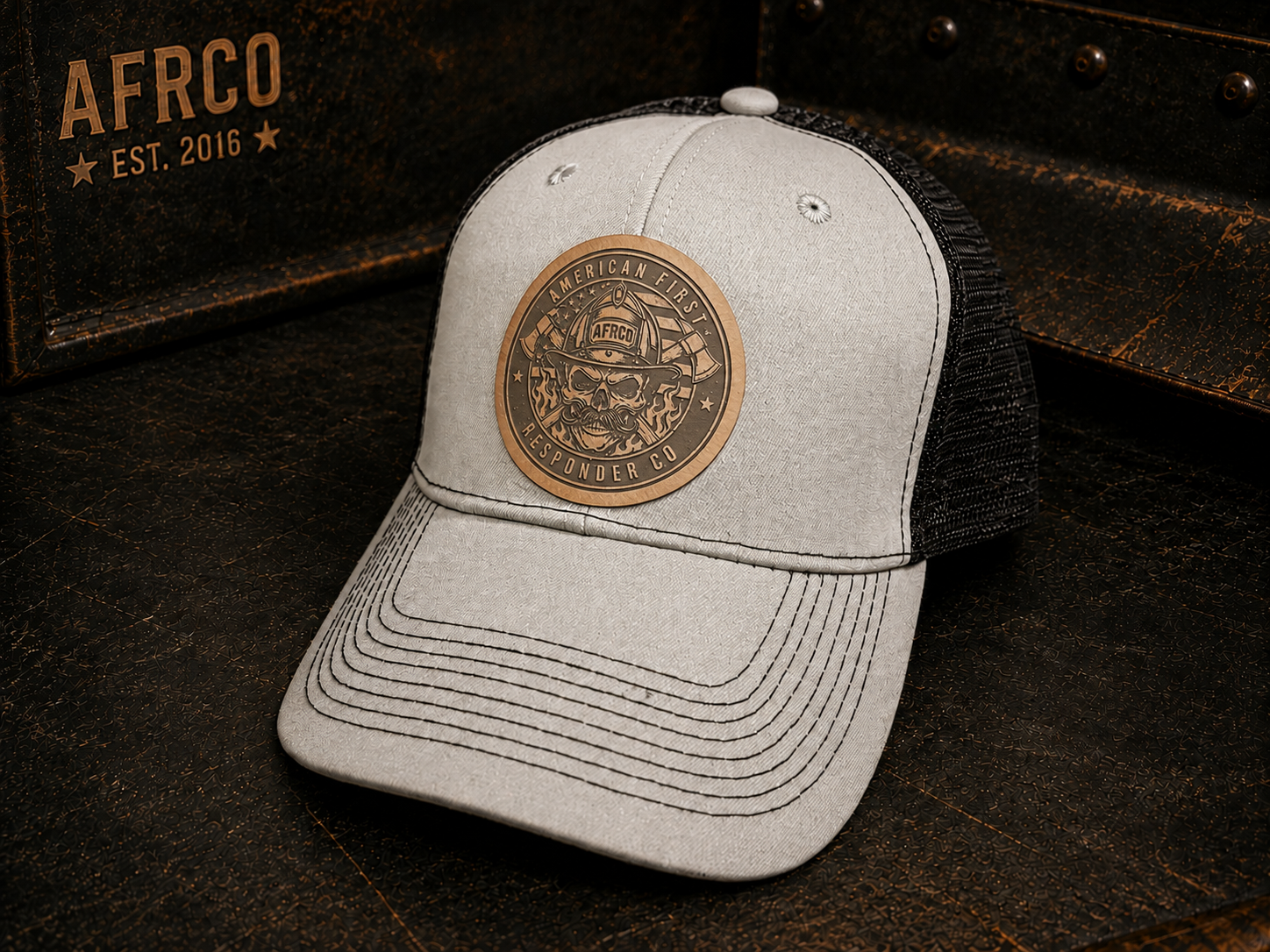 A light gray heather trucker cap with a black mesh back, featuring a circular bronze-toned metal patch on the front with a firefighter skull design and the words 'American Fire Service' and 'LIFELONG FIRE DEPT.'.