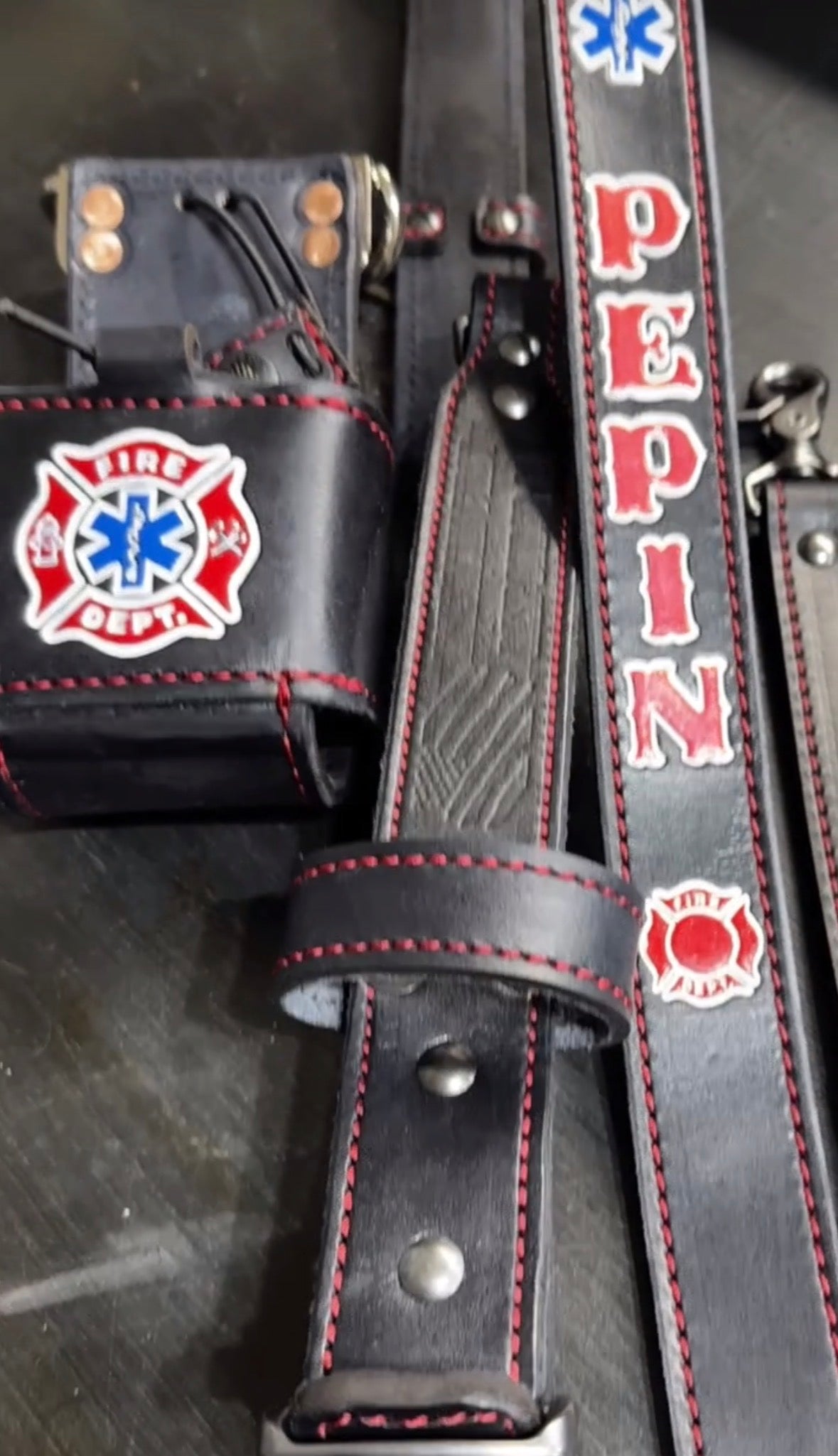 A close-up of a black leather firefighter belt set with red stitching.