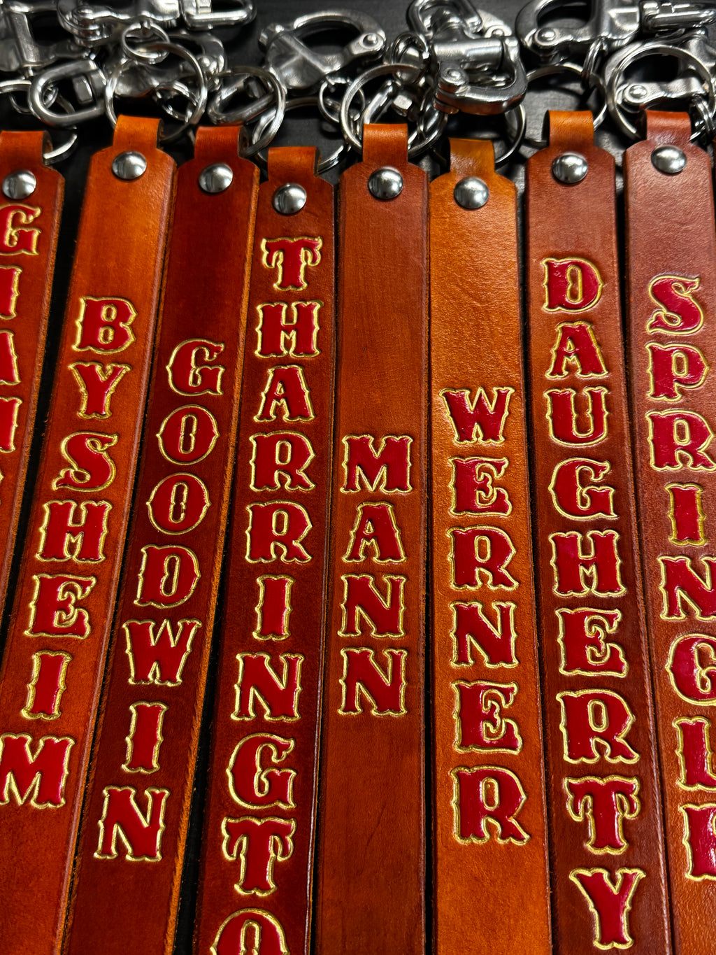 Close-up of custom leather SCBA quick release pulls showing hand-stamped red and gold lettering on full-grain English bridle leather.