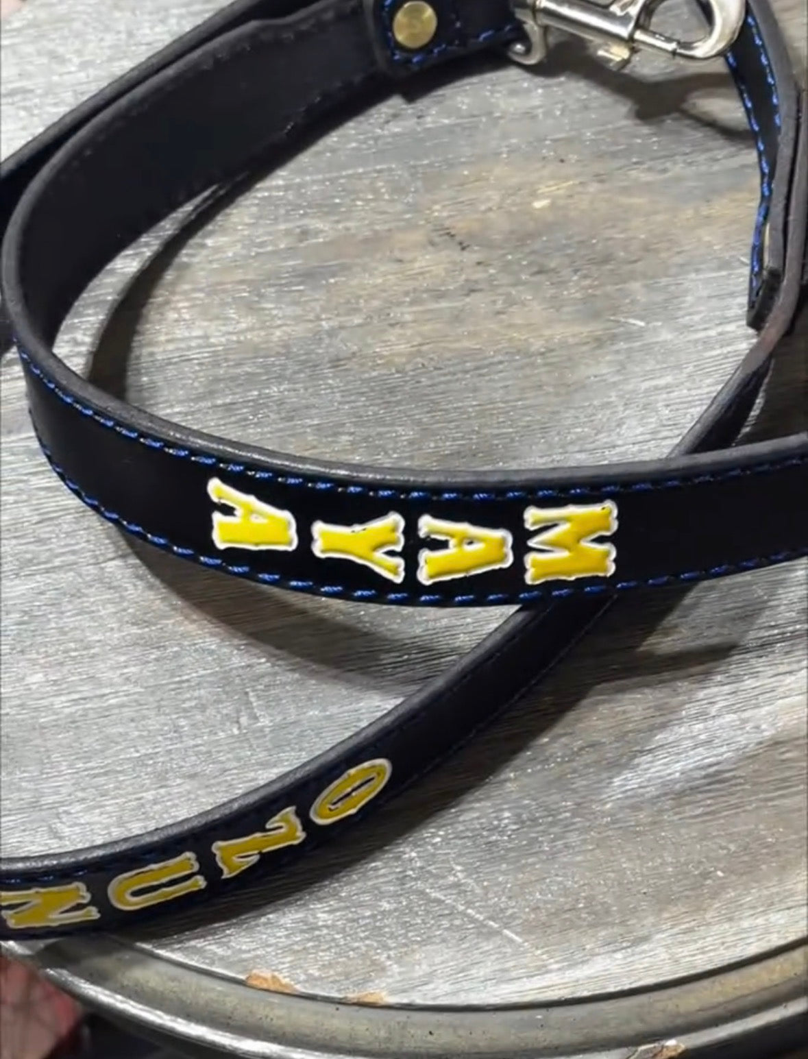 Close-up of a personalized black English bridle leather dog leash with custom stamped name, hand-painted lettering, and heavy-duty swivel snap hardware.