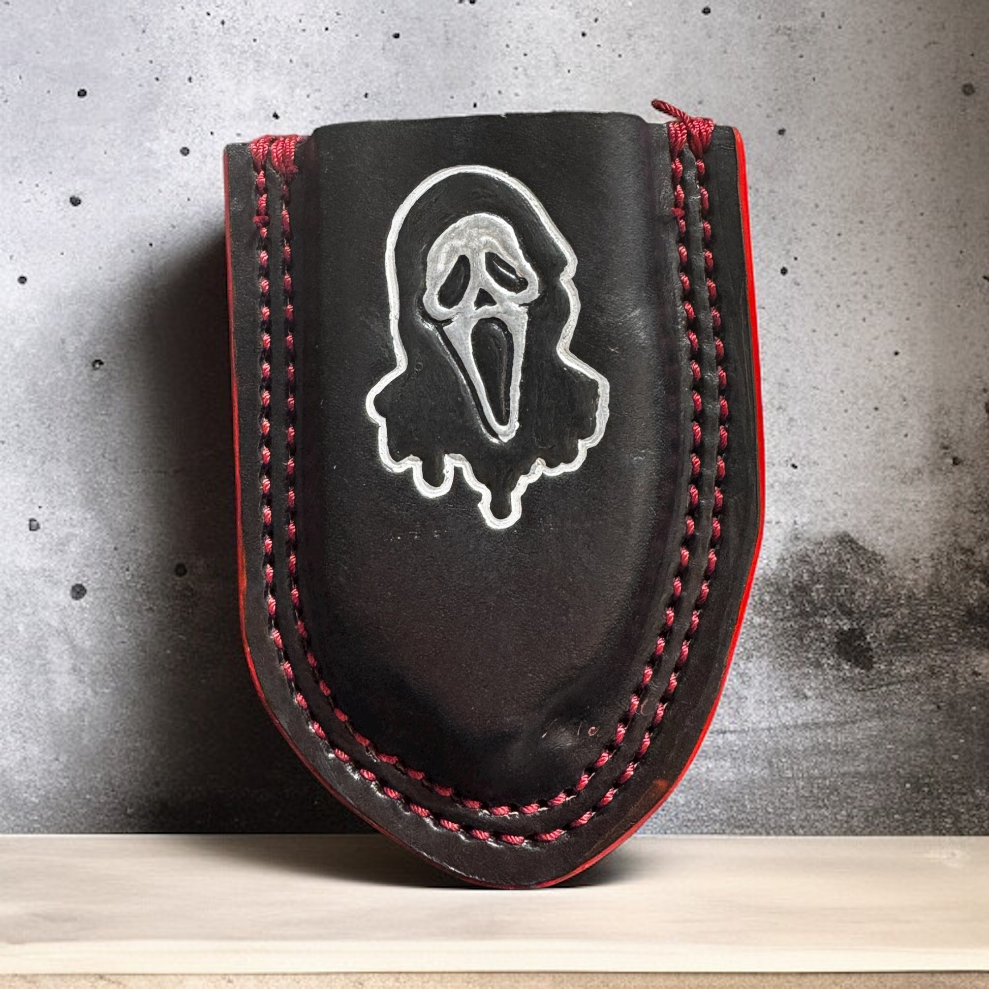 Custom black leather holster for Raptor-style trauma shears with hand-painted horror mask design and red stitched edge detail.