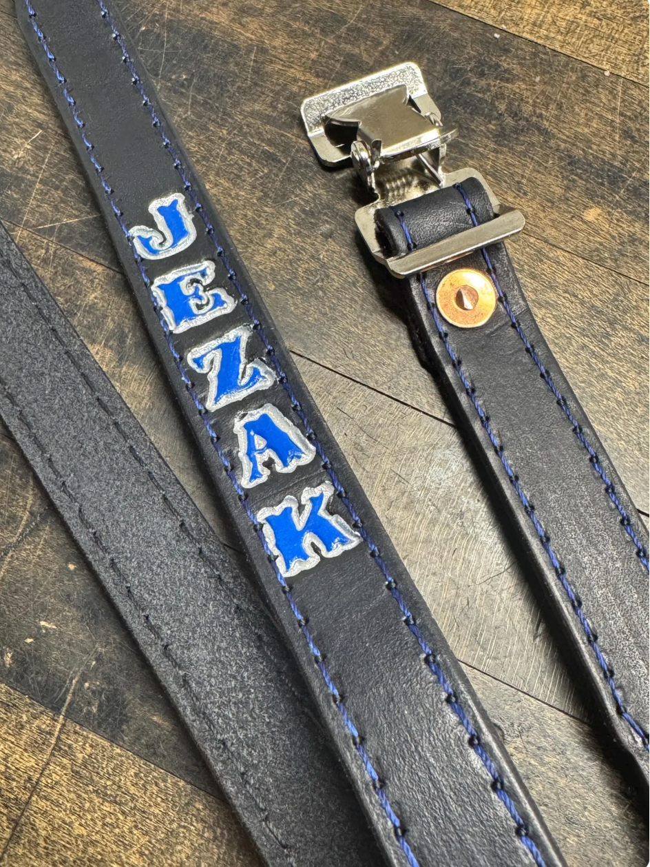 Personalized firefighter helmet chin strap with hand-painted name and blue stitching.