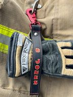 Personalized firefighter glove strap secured to turnout gloves on fire gear.
