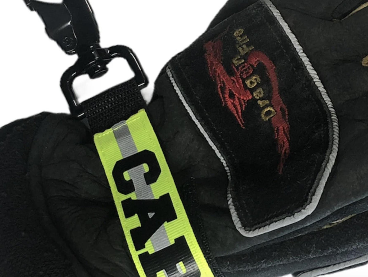 Close up of Personalized firefighter webbing glove strap with yellow reflective name, heavy-duty hardware, and structural firefighting gloves.