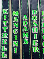 Close-up of personalized glow-in-the-dark leather SCBA quick release pulls showing custom stamped firefighter names and green glow lettering.