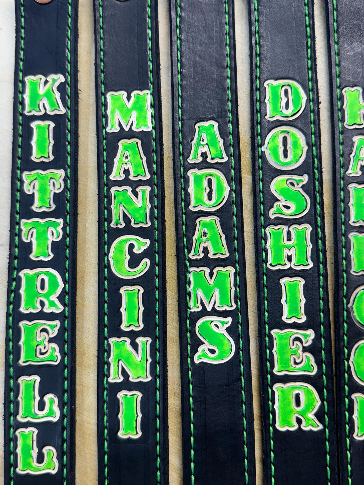 Close-up of personalized glow-in-the-dark leather SCBA quick release pulls showing custom stamped firefighter names and green glow lettering.
